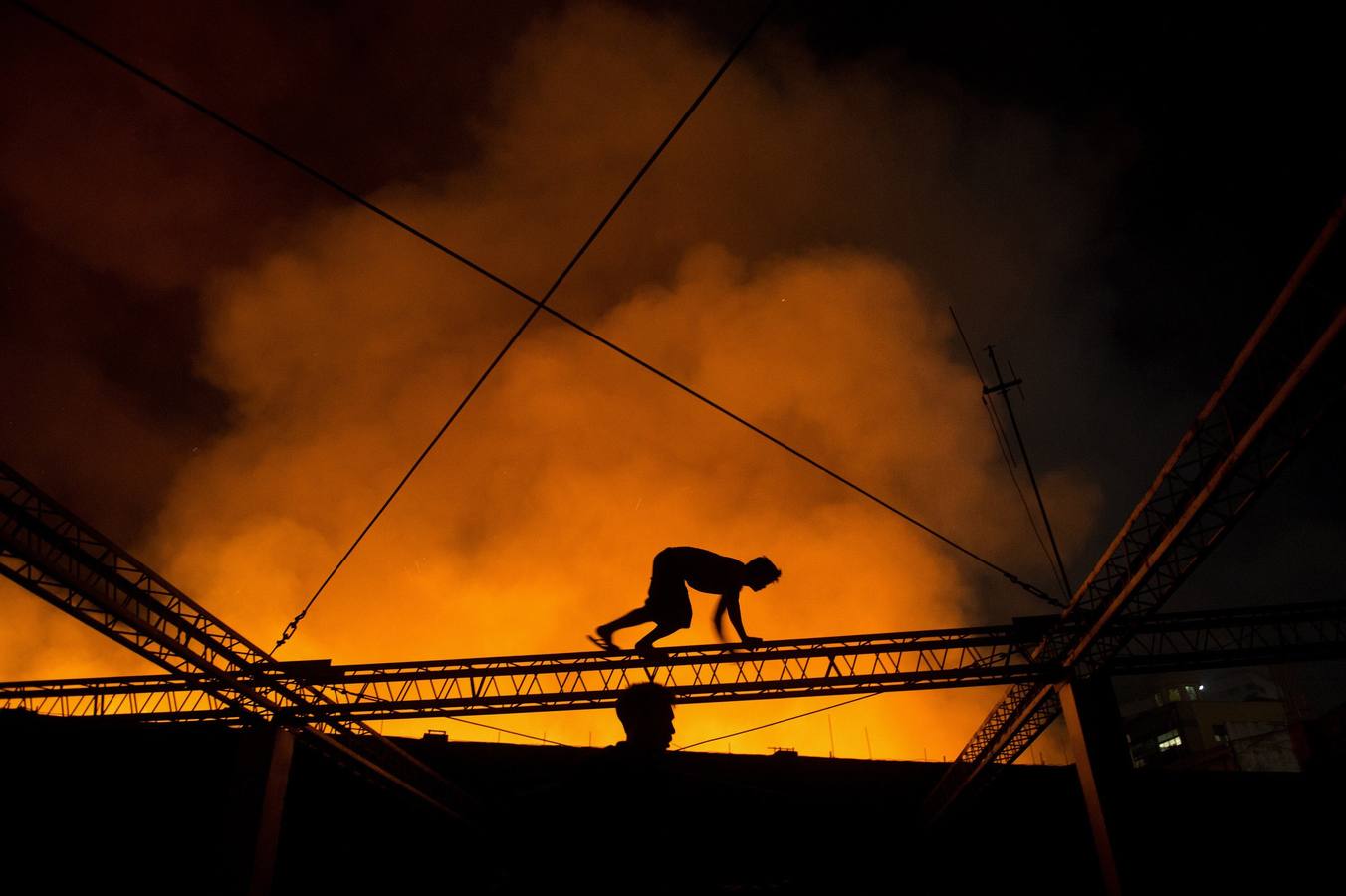 Un hombre se arrastra por un edificio para presenciar un incendio que afectó a un almacén en Manila.