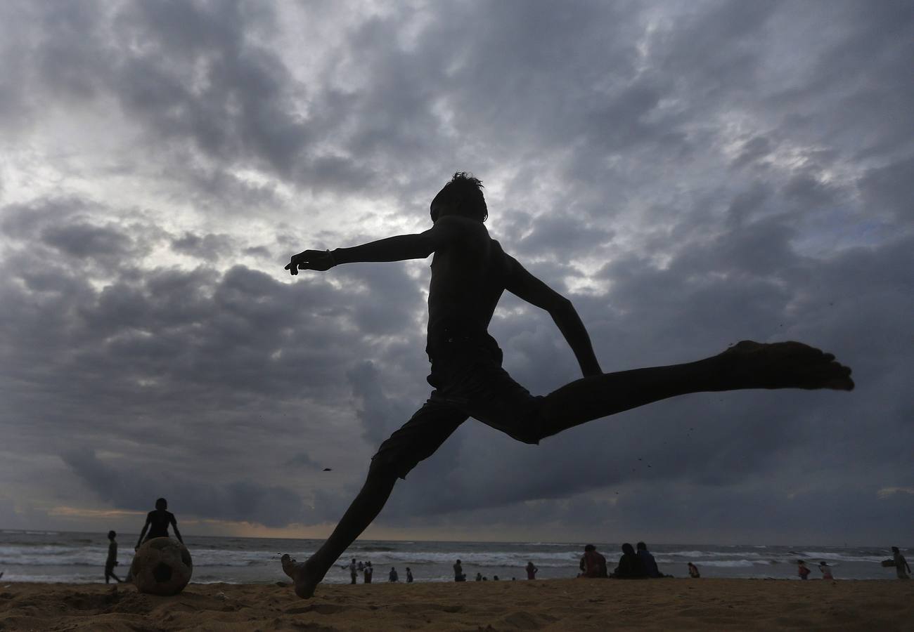 Un niño corre a patear un balón de fútbol en la playa de Colombo.