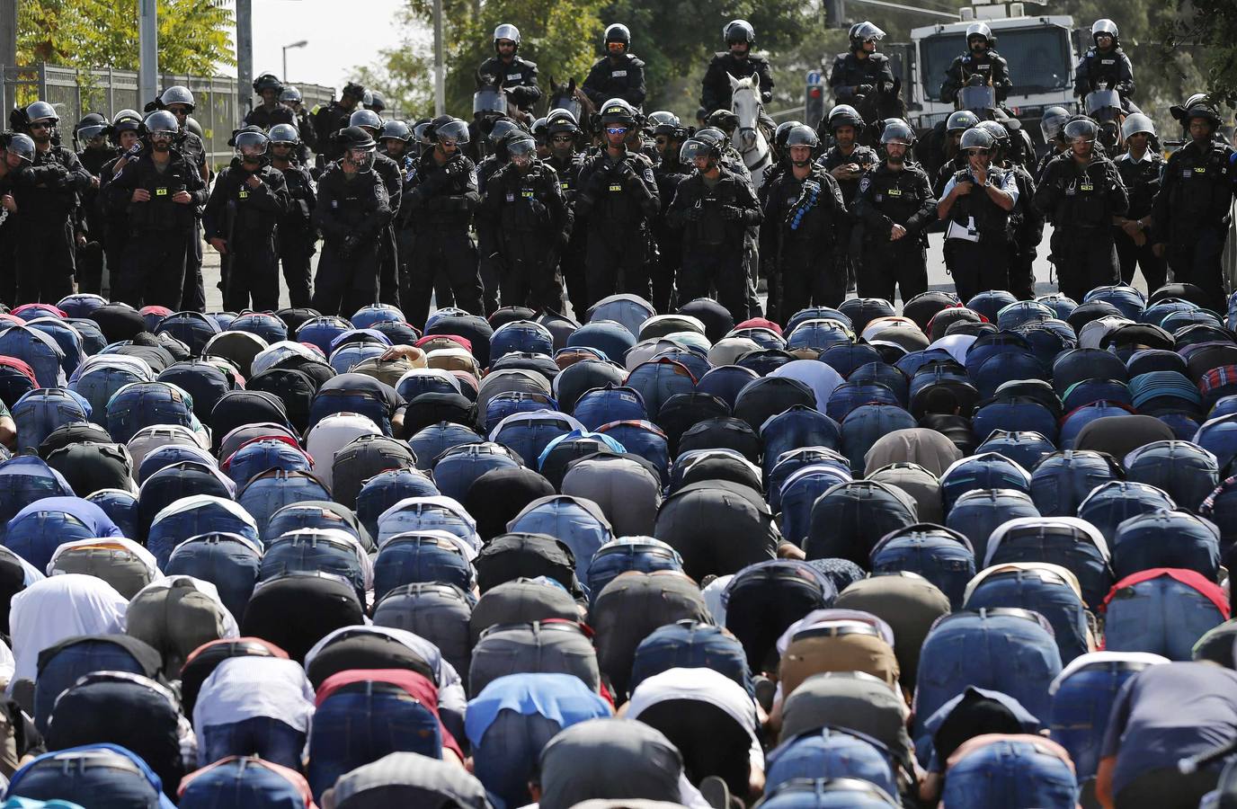 Palestinos rezan mientras los policías israelíes hacen guardia durante las oraciones del viernes en un barrio de Jerusalén.