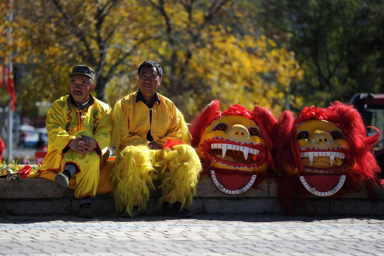 Dos hombres chinos esperan para realizar una danza del león en el inicio de la cuarta etapa del Tour de 2014 de Beijing.