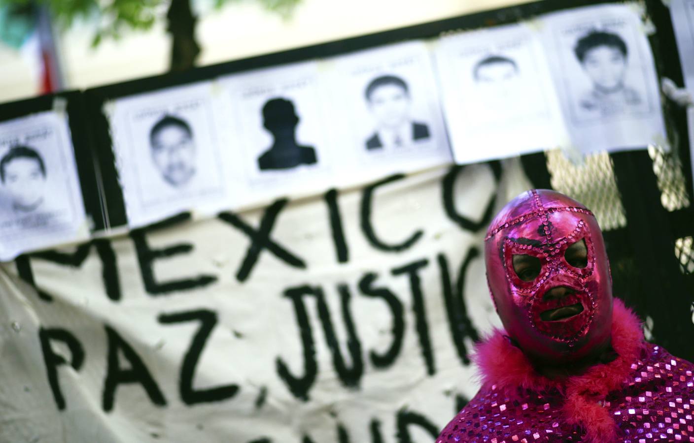 Un hombre vestido como famoso luchador mexicano de Lucha Libre El Santo se pone delante de las imágenes de algunos de los 43 estudiantes que faltan de Ayotzinapa .