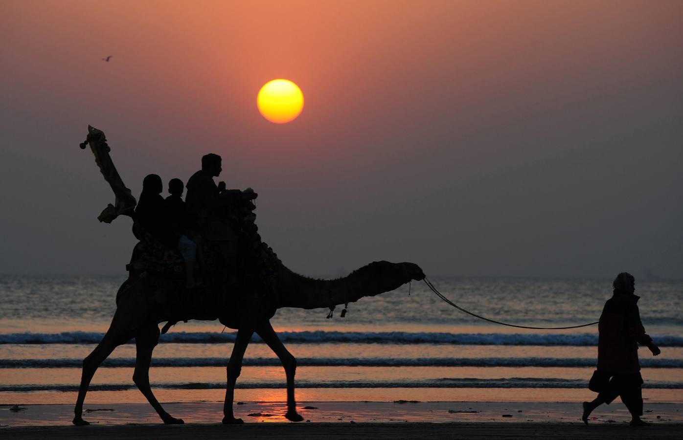 Turistas paquistaníes viajan en un camello durante la puesta de sol en la playa de Clifton en Karachi.