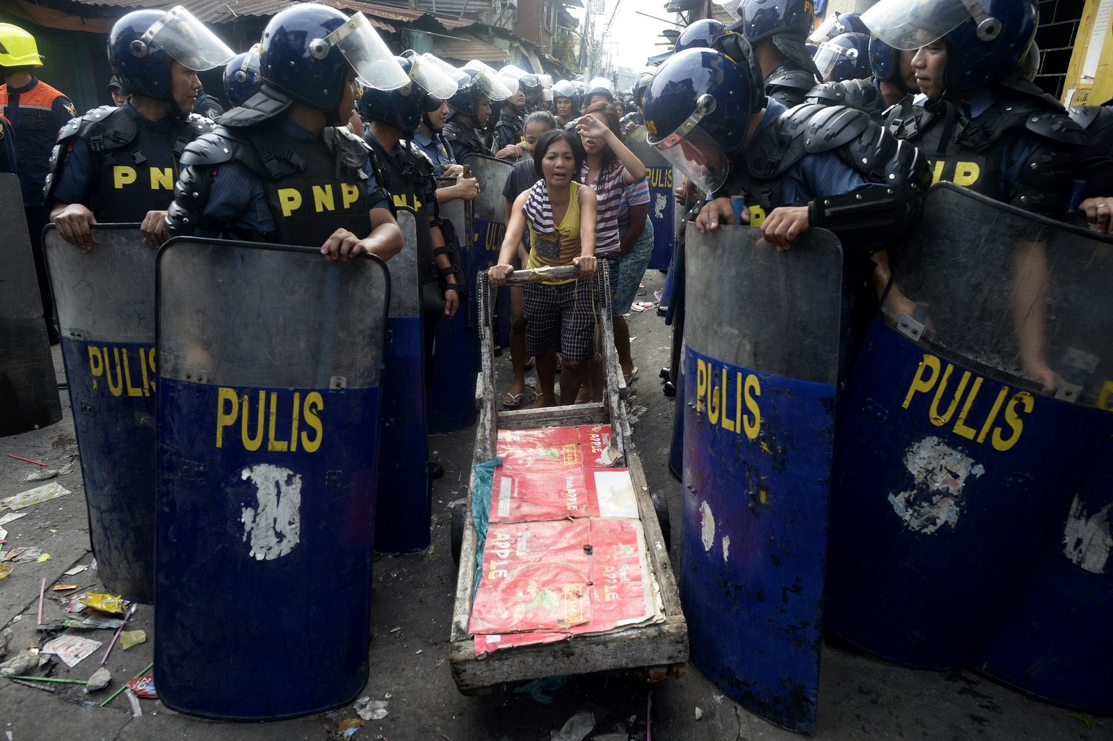 Un residente empuja un carro de madera más allá de una fila de policías para llevar sus pertenencias durante la demolición de una comunidad de colonos en Manila.