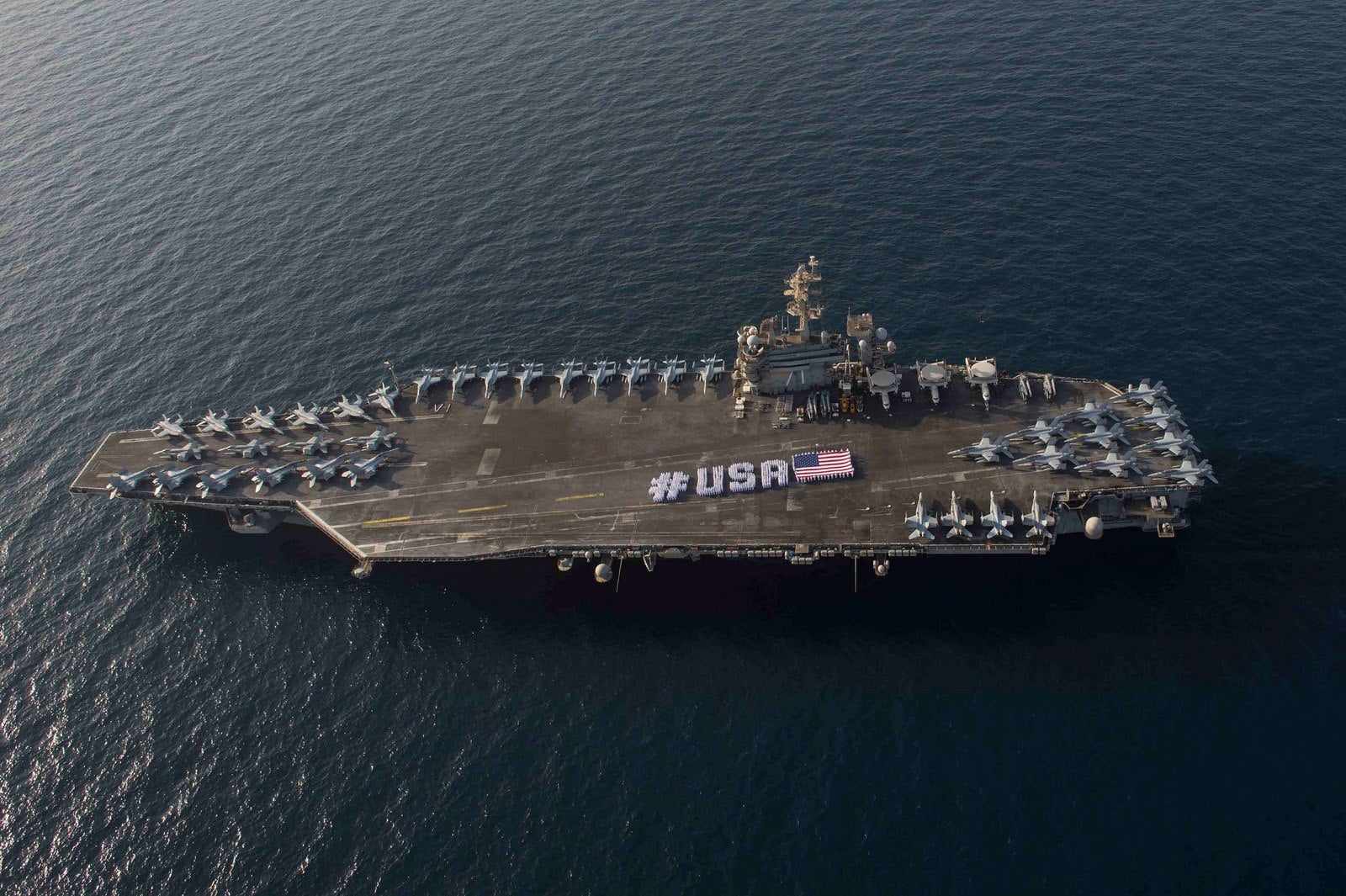 Esta foto US Navy muestra los marineros con la bandera americana en la cubierta de vuelo del portaaviones USS Theodore Roosevelt.