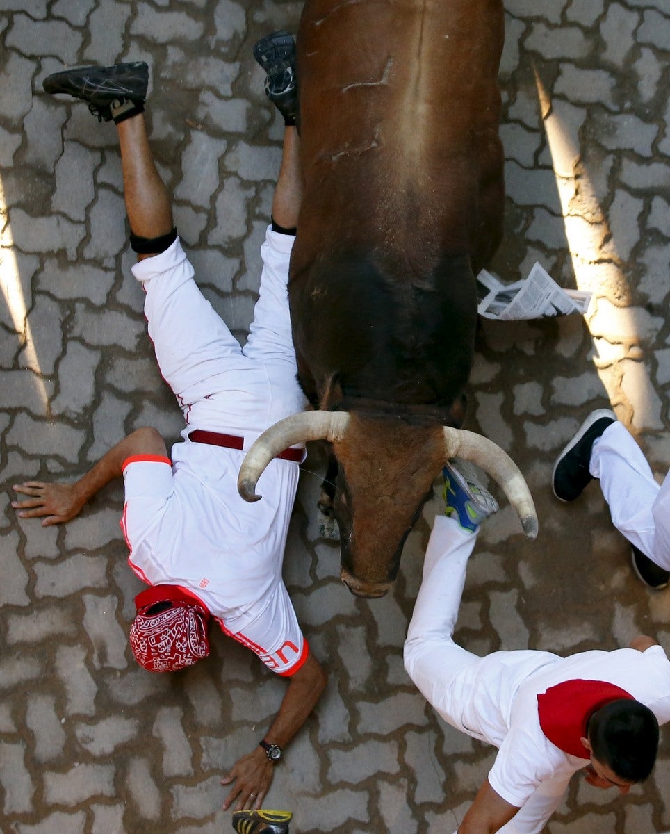 Un corredor cae al lado de un toro en la entrada a la plaza de toros durante el cuarto encierro de los toros en el festival de San Fermín en Pamplona.