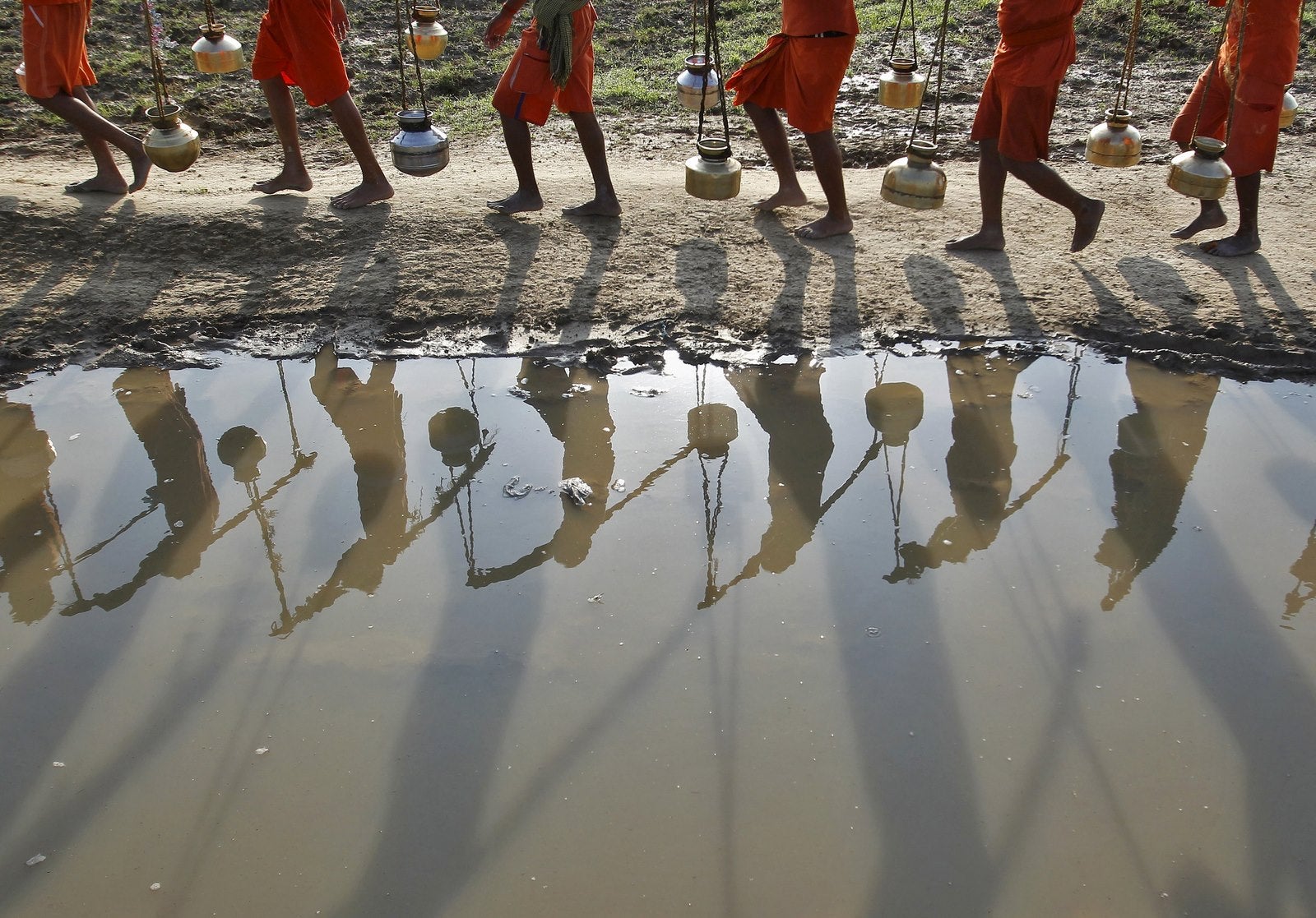 Kanwarias o devotos del dios hindú Shiva se reflejan en un charco, después de llenar las jarras con agua desde el río Ganges en Allahabad, India.