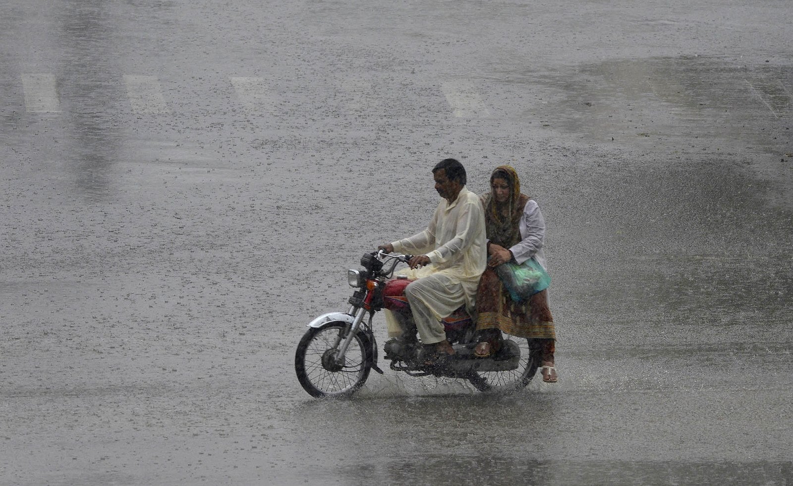 Un paquistaní conduce su motocicleta a través de la lluvia del monzón en Lahore.