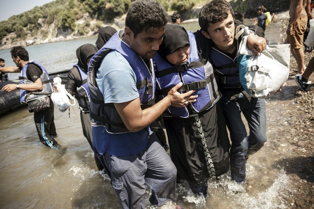 Una mujer es asistida al llegar a la isla griega de Lesbos después de cruzar el mar Egeo, en un bote inflable.