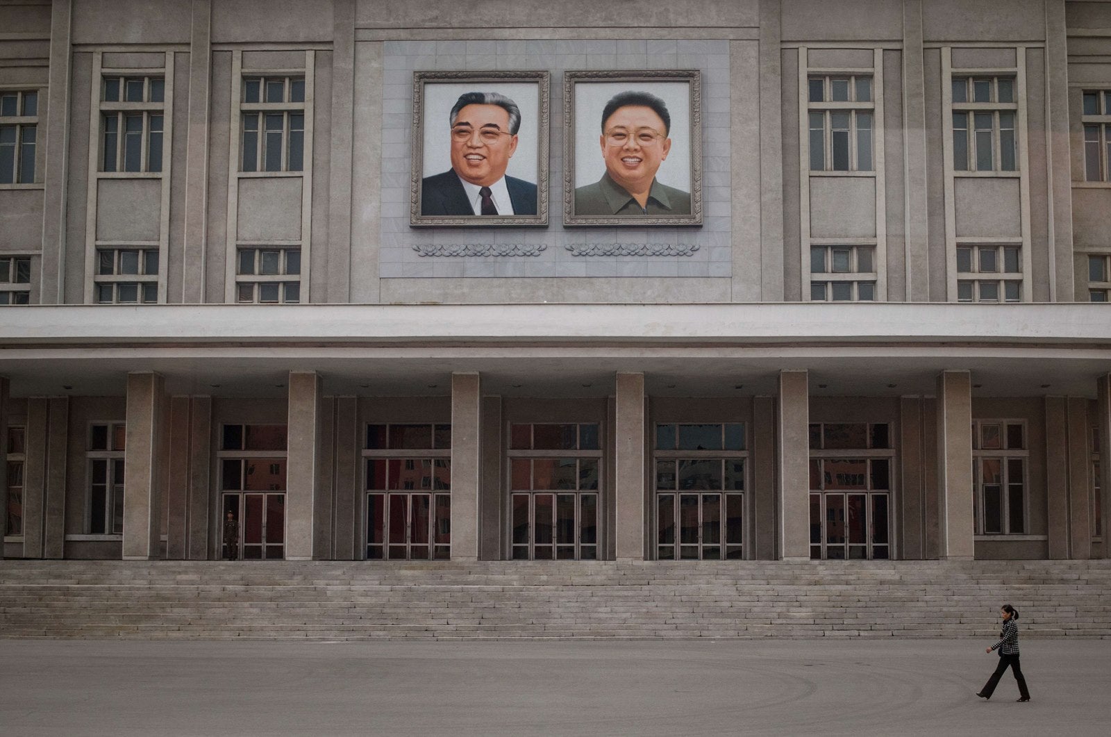 Una mujer camina delante de retratos de los líderes de Corea del Norte a finales de Kim Il-Sung (arriba L) y Kim Jong-Il.