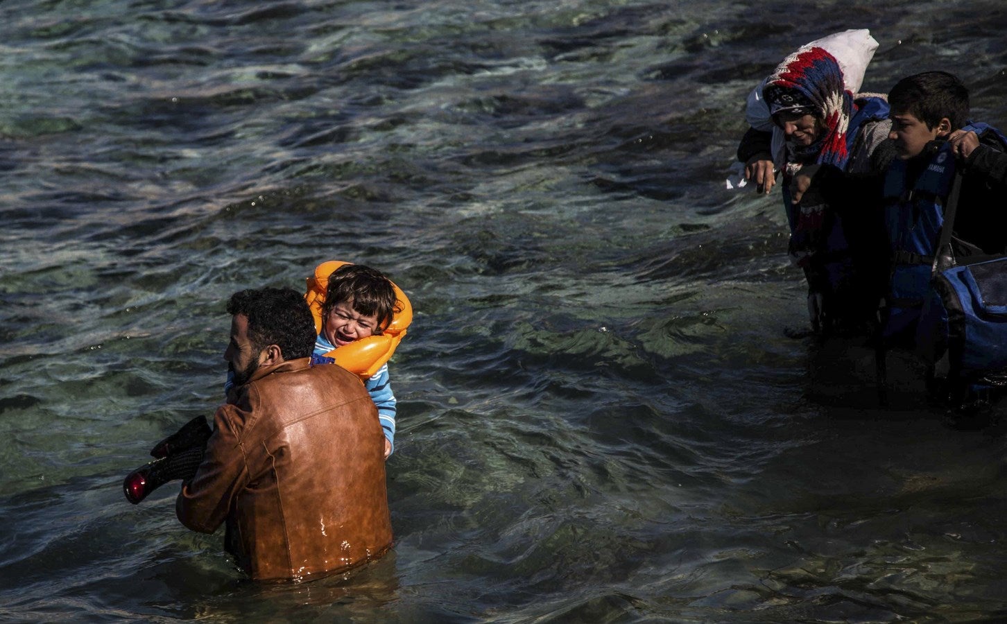 Un hombre lleva en brazos un niño como inmigrantes y refugiados caminan hacia un bote para viajar a la isla griega de Chios de Cesme, en la provincia turca de Izmir.