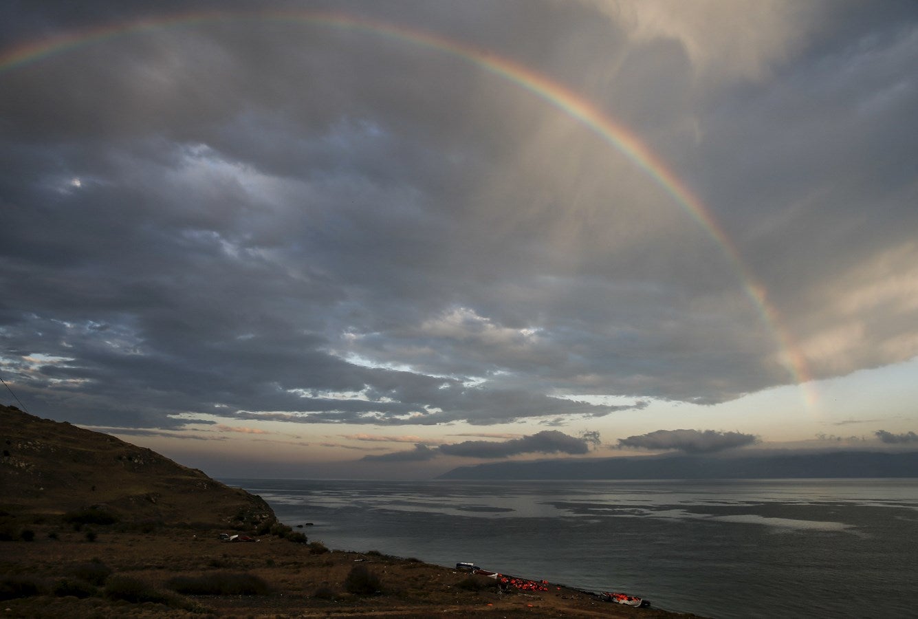 Un arco iris se ve sobre una playa con chalecos salvavidas y un barco, dejados por los refugiados y los inmigrantes que llegaron a la isla griega de Lesbos.