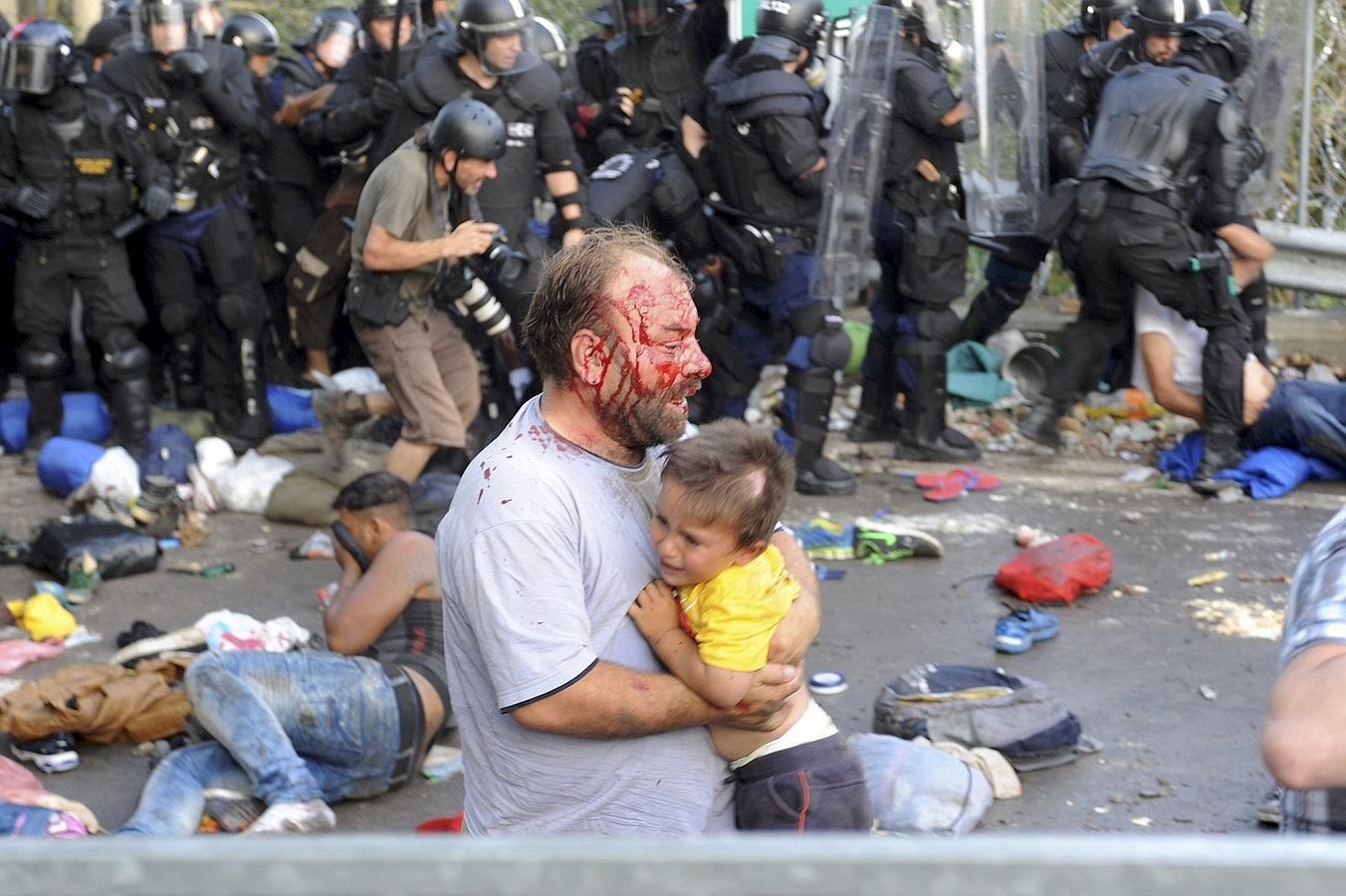 Un inmigrante herido lleva a un niño durante los enfrentamientos con la policía antidisturbios húngaros en el cruce fronterizo con Serbia en Röszke, Hungría.