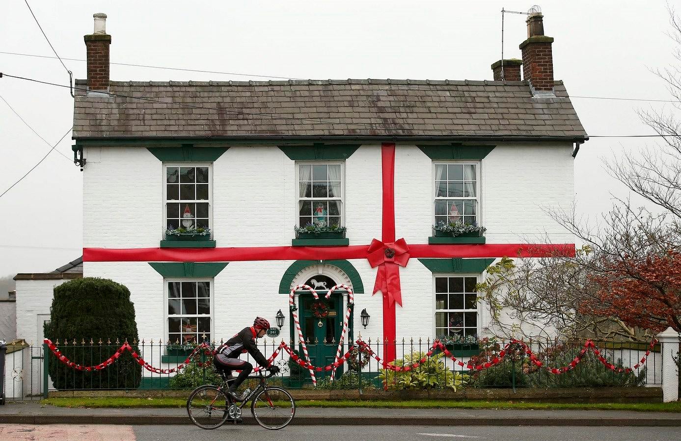 Un hombre sobre una bicicleta pasa delante de una casa decorada como un regalo de Navidad en Académico verde, norte de Gran Bretaña.