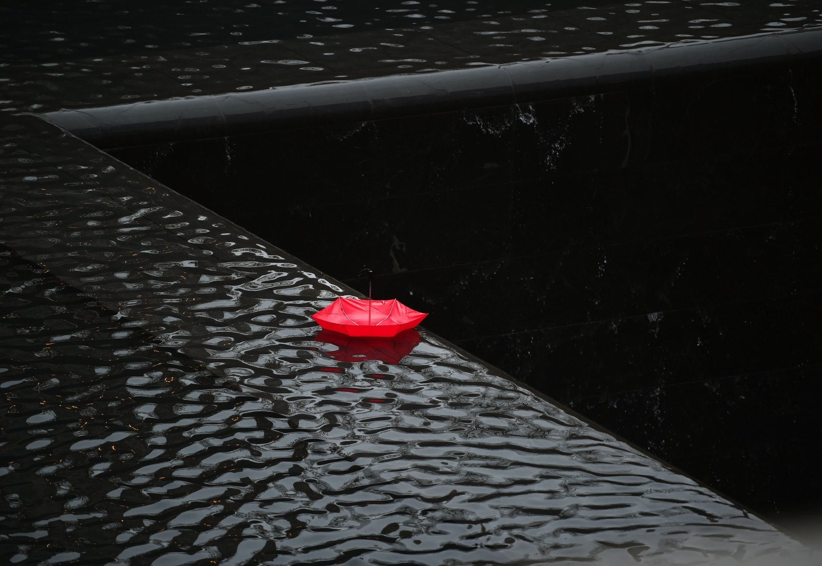 Un paraguas rojo cuelga en el borde de la cascada de la piscina de la torre sur en el 9/11 Memorial Plaza en Nueva York.