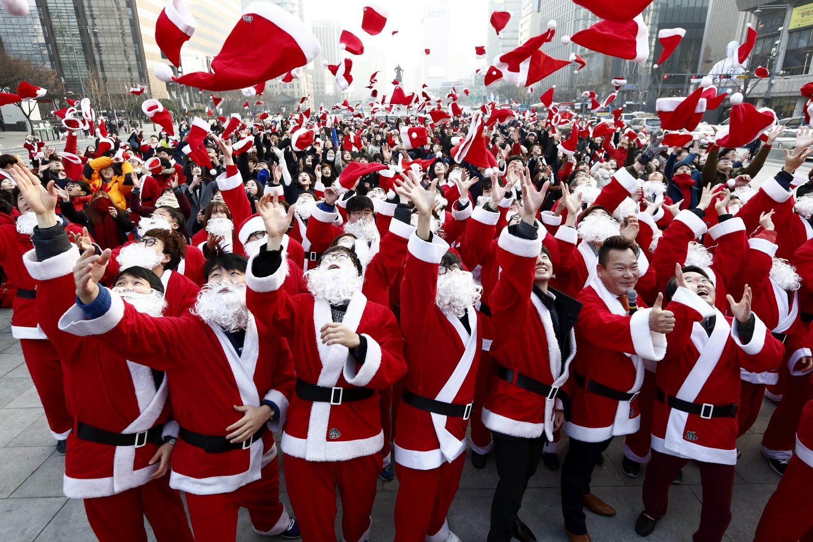 Voluntarios surcoreanos vestidos de Papá Noel Lanzan al aire sus gorros Durante un acto solidario en la plaza de Gwanghwamun de Seúl (Corea del Sur).