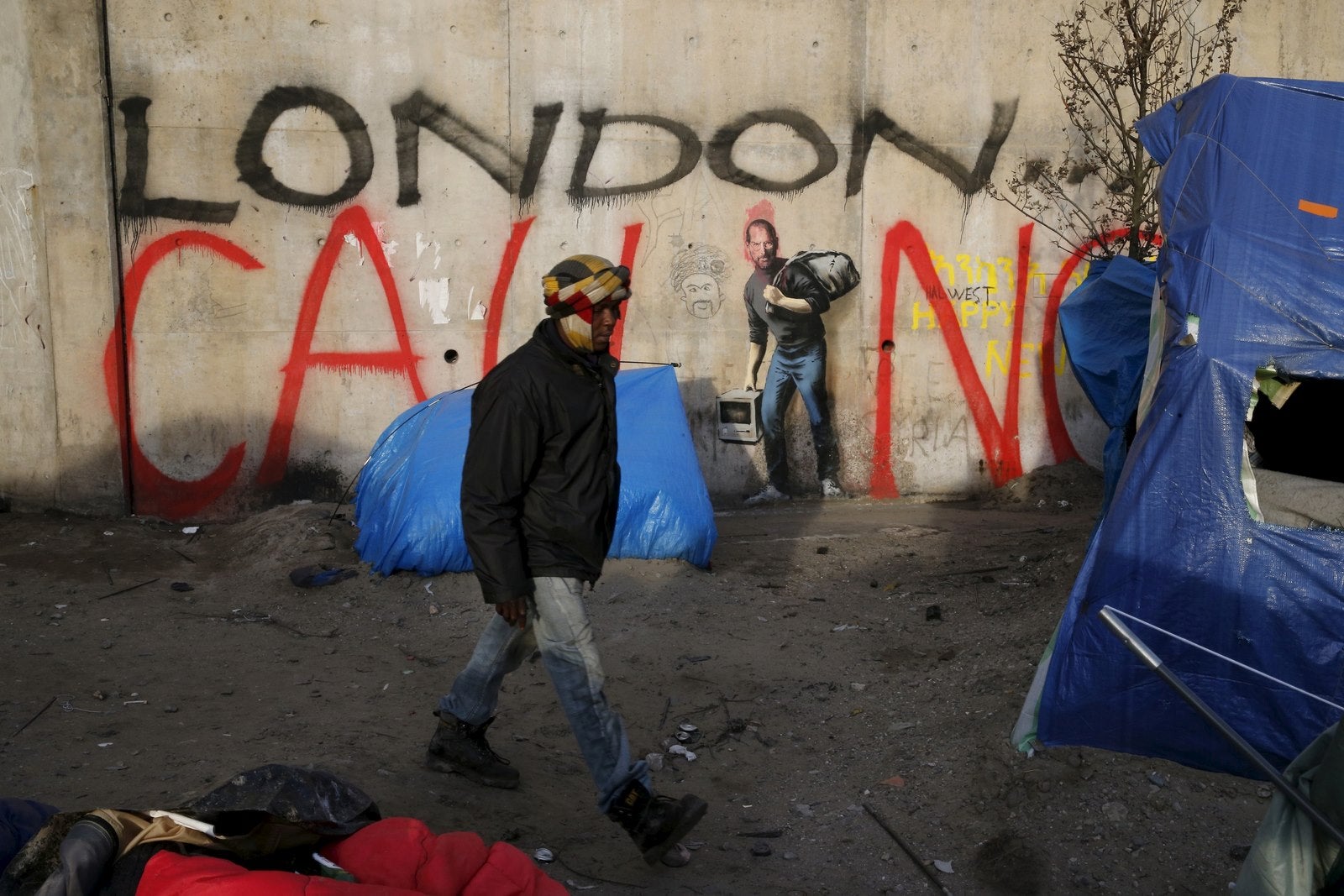 Un migrante pasa junto a una pared con un mural de graffiti en representación de Steve Jobs por el artista británico Banksy en la "nueva jungla", un campo donde los migrantes y solicitantes de asilo permanecen en Calais, Francia.