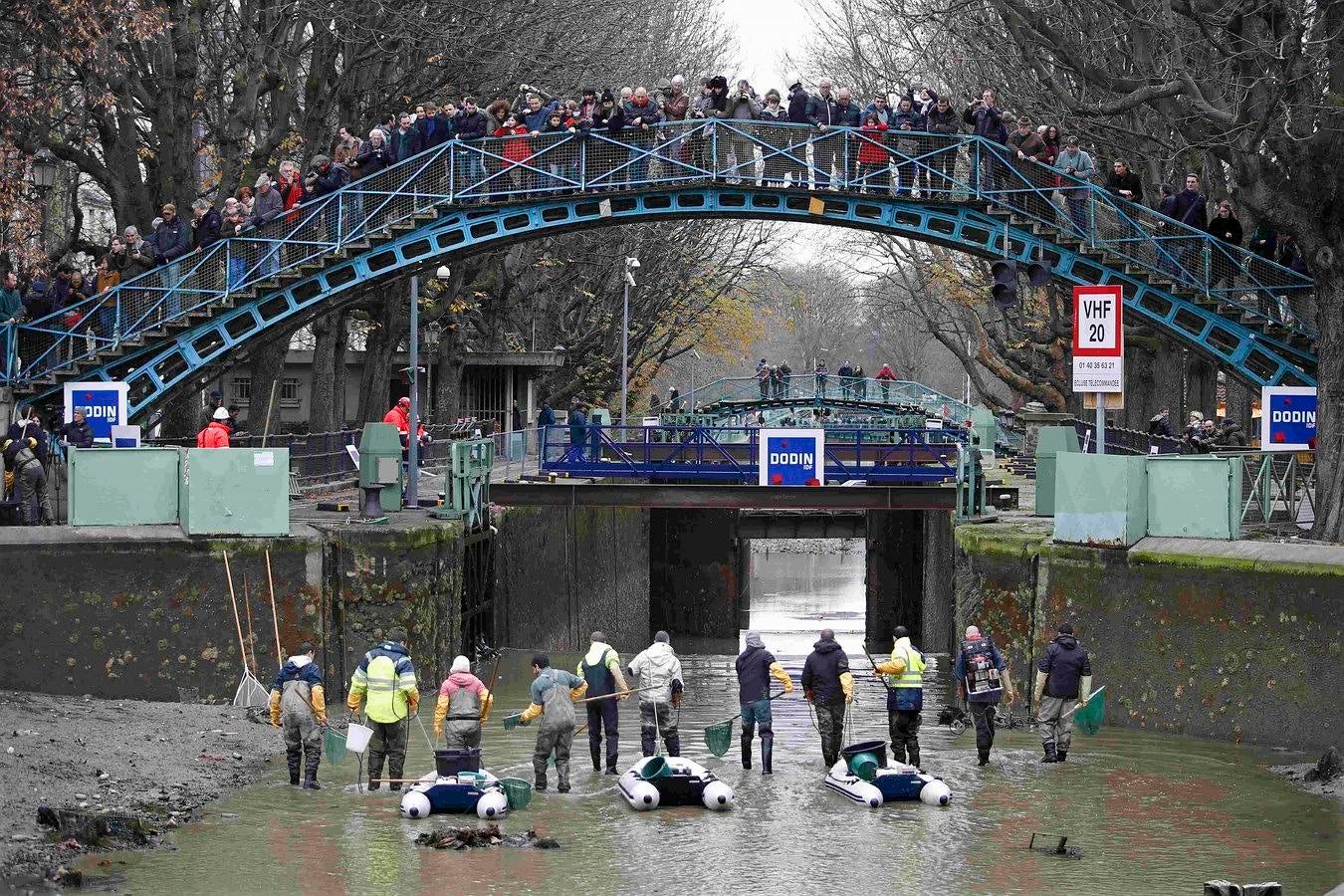 Los periodistas y transeúntes observan como los trabajadores limpian el Canal Saint-Martin en París, Francia.