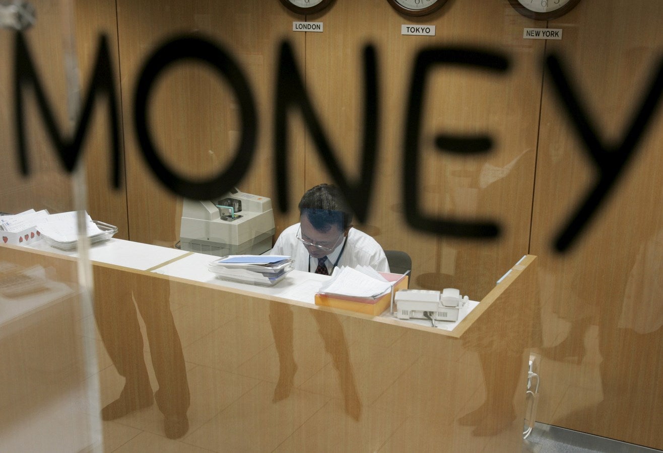 Una línea de clientes esperando se reflejan en una ventana mientras un empleado cuenta el dinero en el Banco de Tokio-Mitsubishi UFJ.