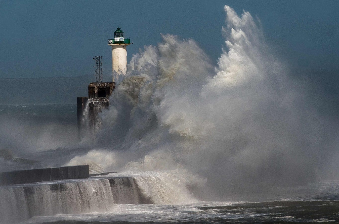 Una ola rompe contra un muelle en frente de un faro en Boulogne-sur-Mer.