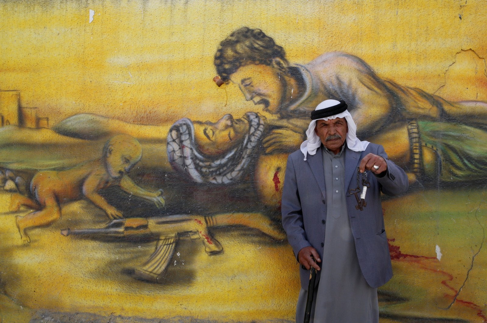 Refugiado palestino Shaher al Khatib, de 76 años, tiene las llaves que simbolizan la pérdida de su casa mientras posa para una fotografía delante de un mural.