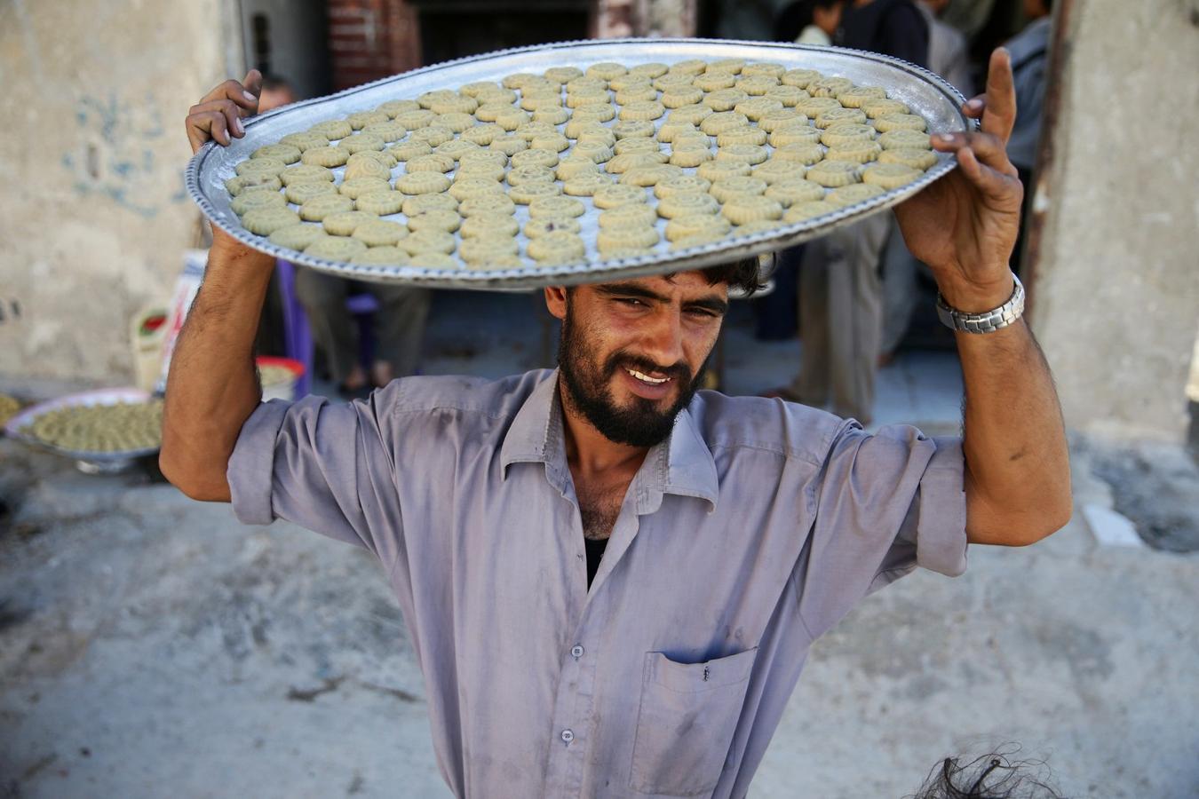 Un hombre lleva una bandeja con dulces tradicionales en la cabeza que marca el fin del Ramadán en la ciudad de Douma, Ghouta oriental en Damasco, Siria sitiada