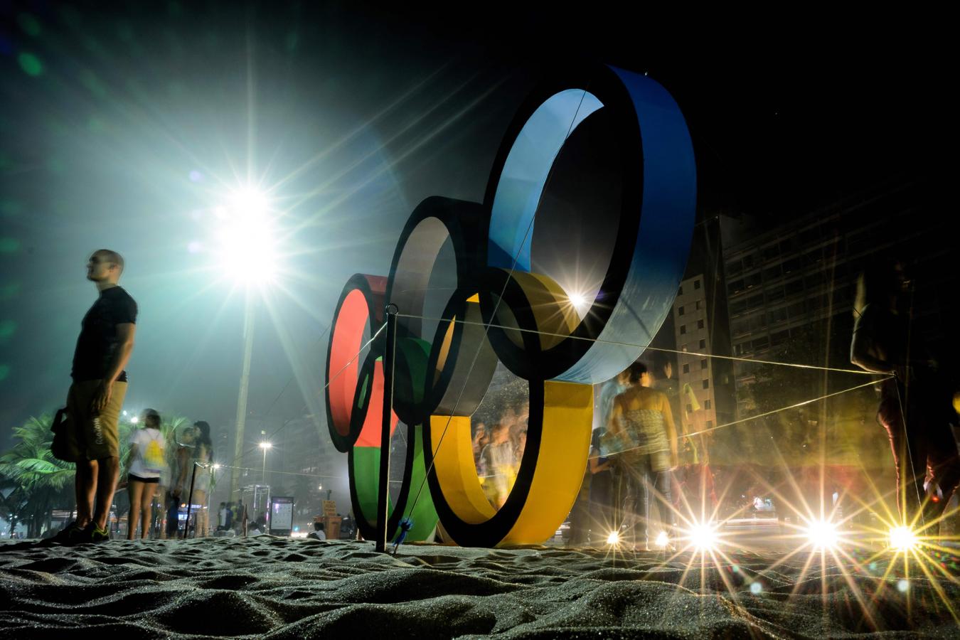 Las personas posan para fotografías cerca de una gran pantalla Anillo Olímpico en la playa de Copacabana en Río de Janeiro