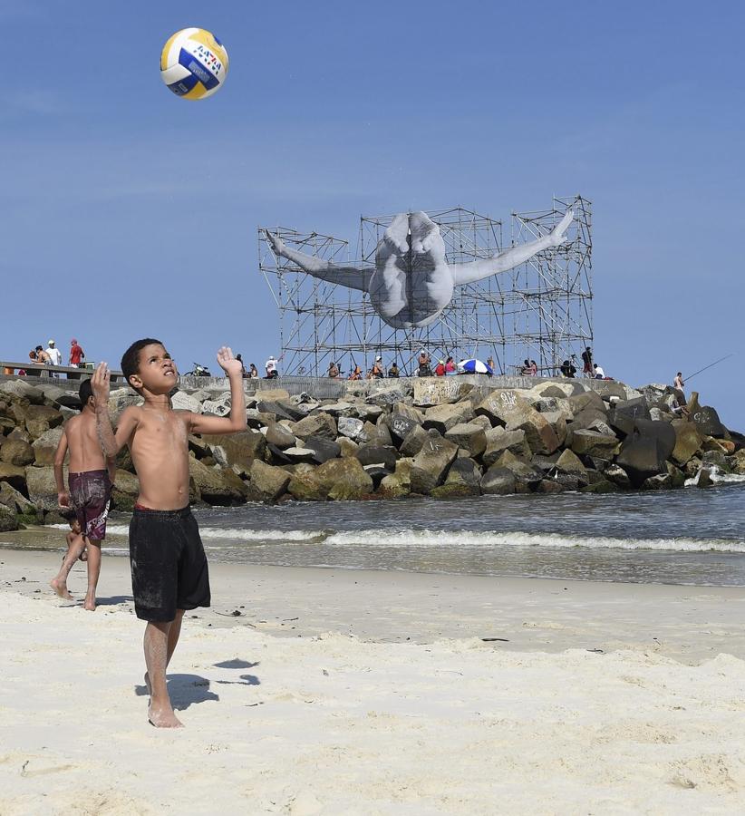 Niños juegan al fútbol en la playa de Barra junto a una obra de arte callejero por el artista francés JR representa al buceador brasileño Cleuson Lima Do Rosario. (Brasil)