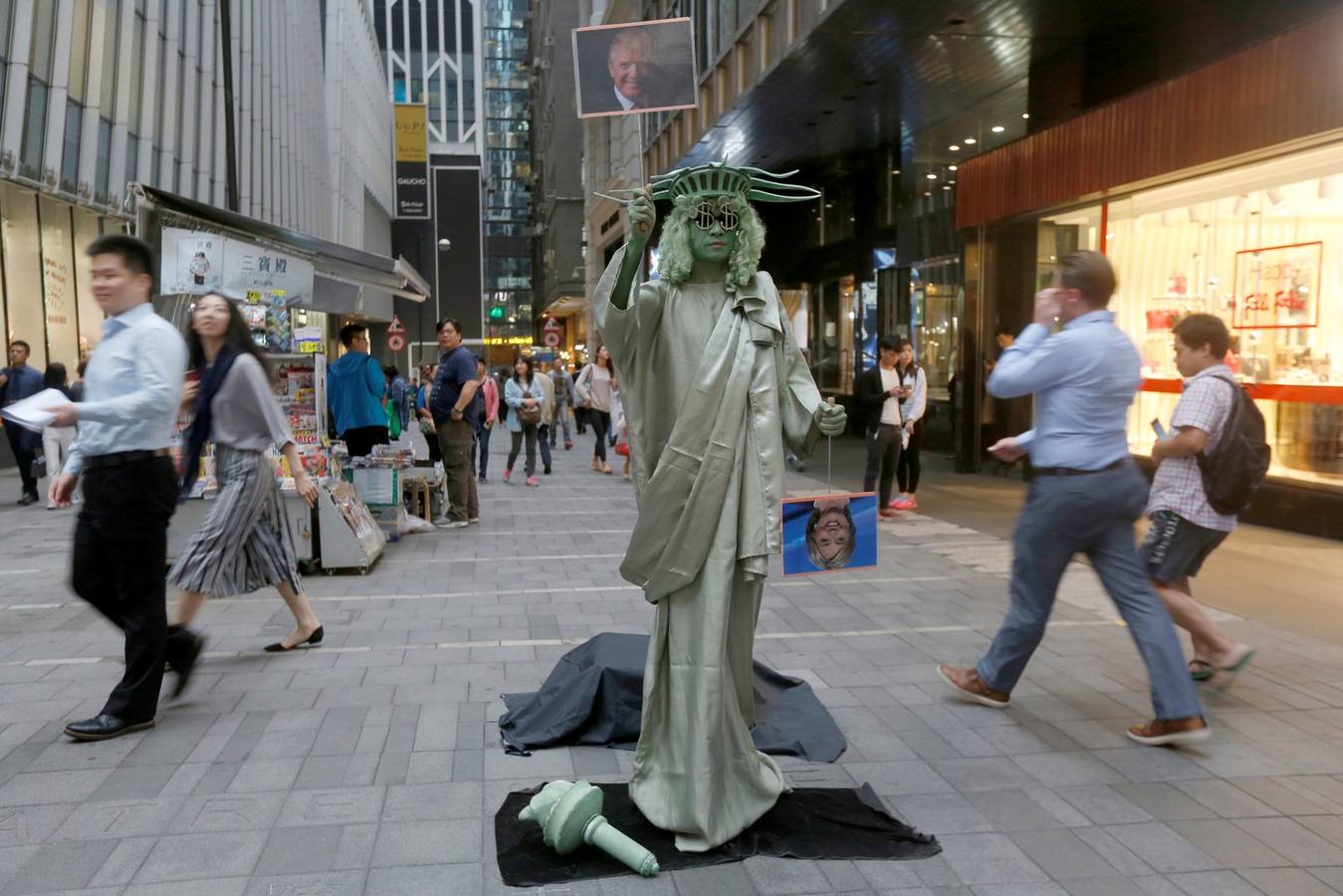 Un artista callejero vestido como estatua de la libertad lleva las fotos de los candidatos presidenciales en el distrito financiero central en Hong Kong.