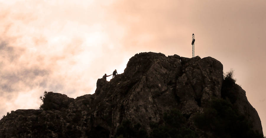 Dos montañeros ascienden entre las rocas para llegar hasta el risco en el que se ubica la cruz de hierro conocida como Cruz de Víznar.