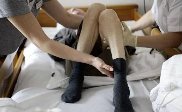 Enfermeras de una residencia mueven las piernas de un anciano que se encuentra en estado vegetativo