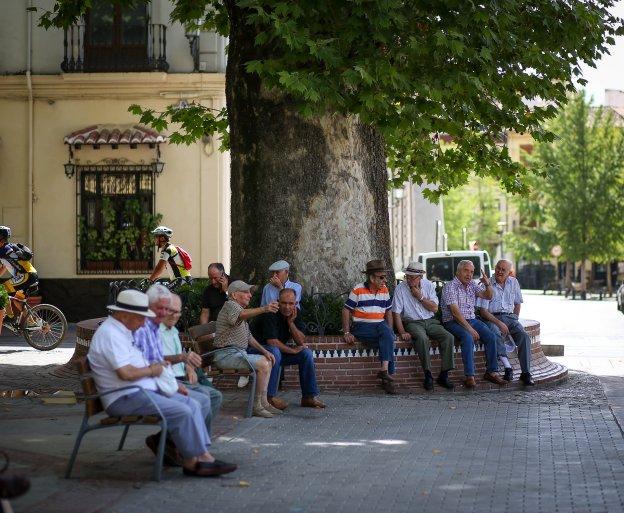 Un grupo de mayores se reúne bajo la amplia sombra de la plaza del Campillo, junto a la Fuente de las Batallas.