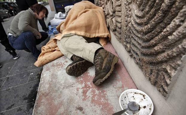 Una integrante de un servicio social de emergencias para gente sin hogar entrega un saco de dormir a un hombre sin techo.