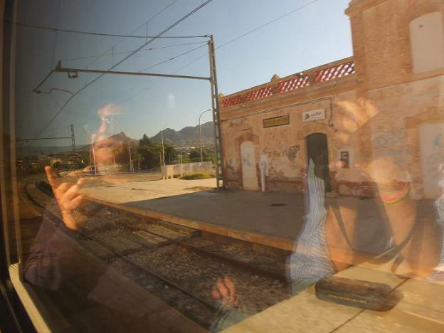 Un pasajero señala con el dedo -al trasluz del cristal de un tren- a la estación de Benahadux-Pechina, en desuso desde los años noventa.