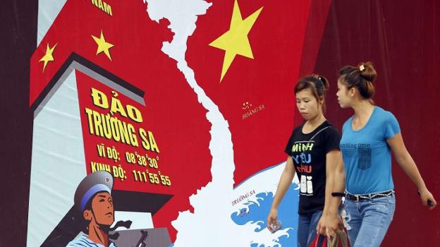 Dos mujeres pasan ante un mural alusivo al conflicto fronterizo entre China y Vietnam en Hanoi. Abajo, la polémica prenda de GAP. 