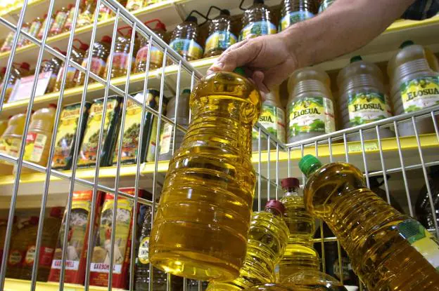 Un joven guarda una botella con aceite de oliva en el carro de la compra. 