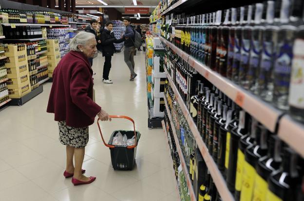 Una mujer observa estanterías con productos en un supermercado ante la mirada de unos jóvenes. 