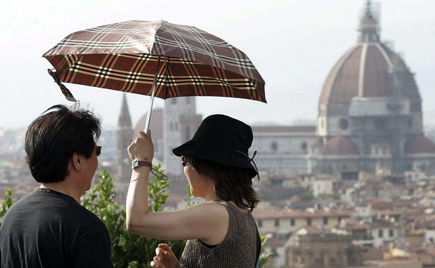 Una pareja de turistas protegiéndose del sol, con el Duomo de Florencia de fondo.