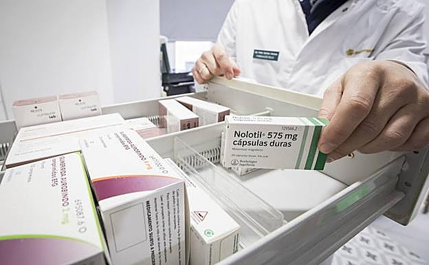 Un farmacéutico coge una pequete de pastillas de un cajón para dispensarla a un usuario.