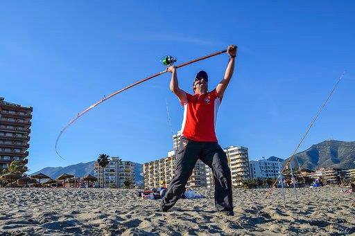 Uno de los participantes lanza su caña al agua, sobre la arena de la Playa de Fuengirola.