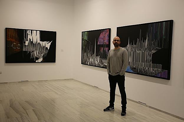 El artista granadino David Trujillo, ante dos de las obras que expone en La Madraza.