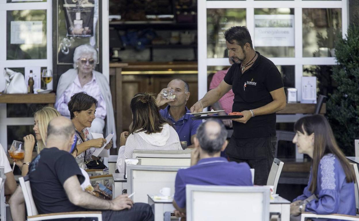 Un camarero atendiendo unas mesas de una terraza de un bar. 