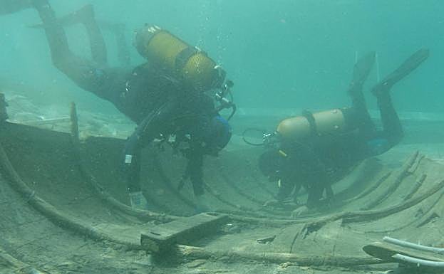 Dos buceadores inspeccionan el casco de la embarcación fenicia. 