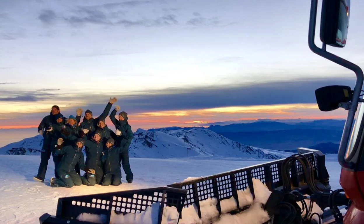 Un grupo de amigos, tras subir a las cumbres de la estación de esquí en una máquina pisa pistas con el atardecer a sus espaldas.