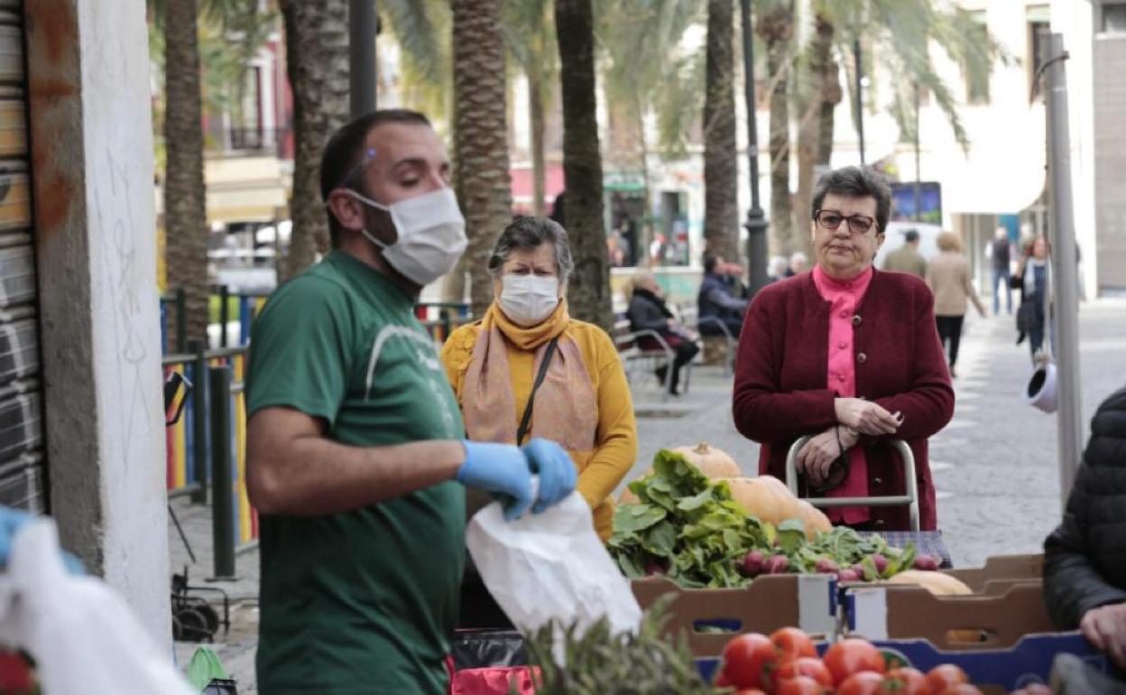 Un tendero atiende con mascarilla a sus clientas en La Romanilla. 