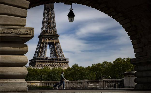 Una mujer con mascarilla pasea cerca de la Torre Eiffel en París