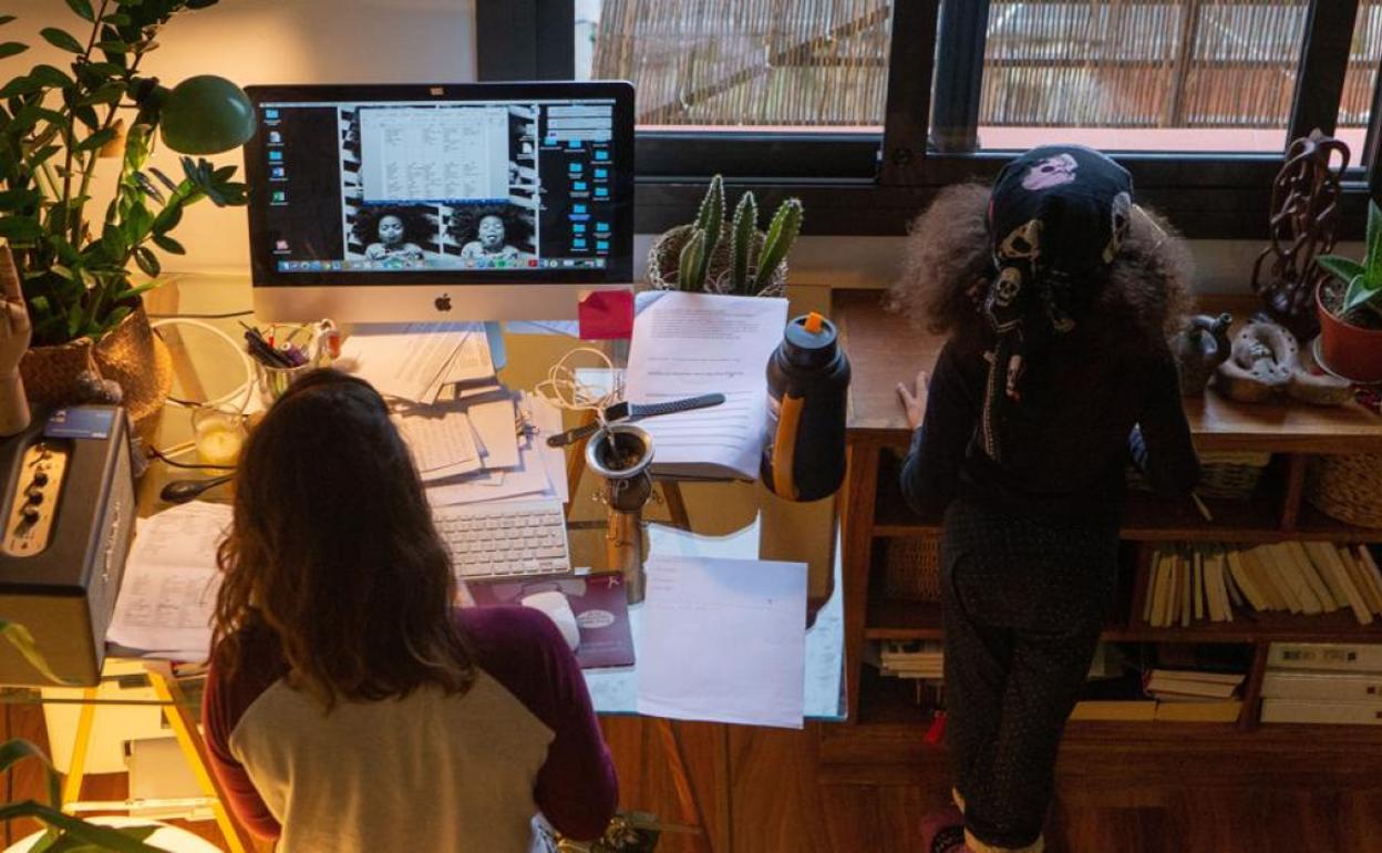 Una mujer realiza teletrabajo en su casa mientras su hija juega a su lado- 