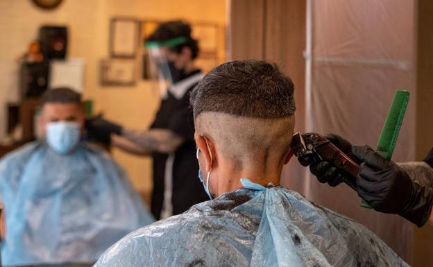 Un peluquero y un cliente, protegidos ambos con diferentes mascarillas en Huelva.