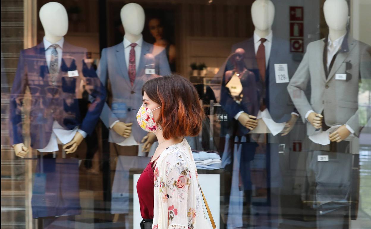 Una mujer protegida con mascarilla pasa junto a una tienda de trajes. 