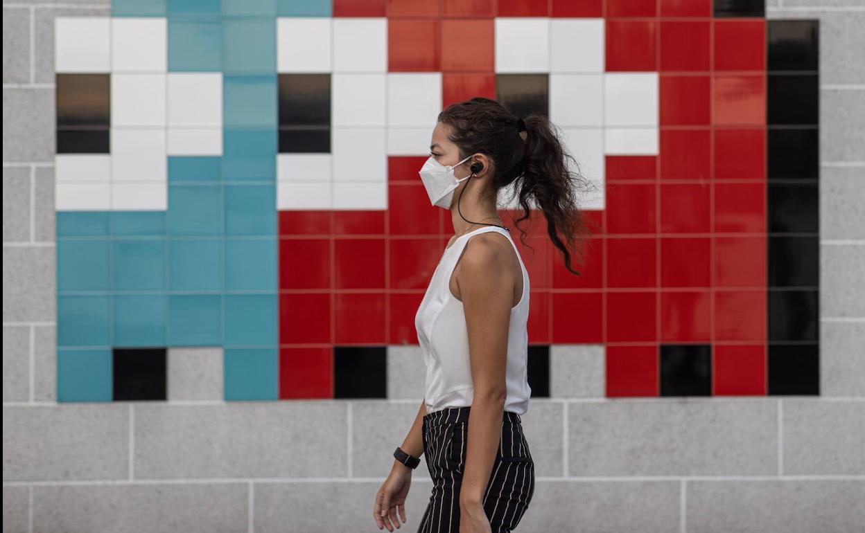 Una mujer camina por la calle con la mascarilla en la cara.