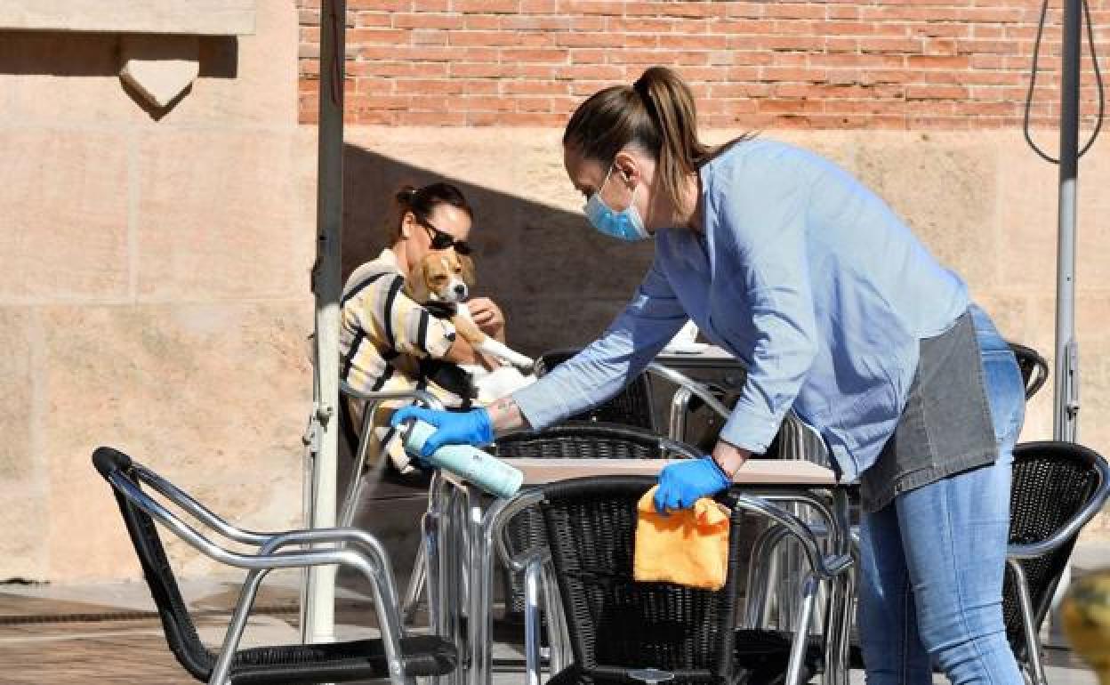 Una camarera desinfecta mesas y sillas en una terraza para recibir nuevos clientes.